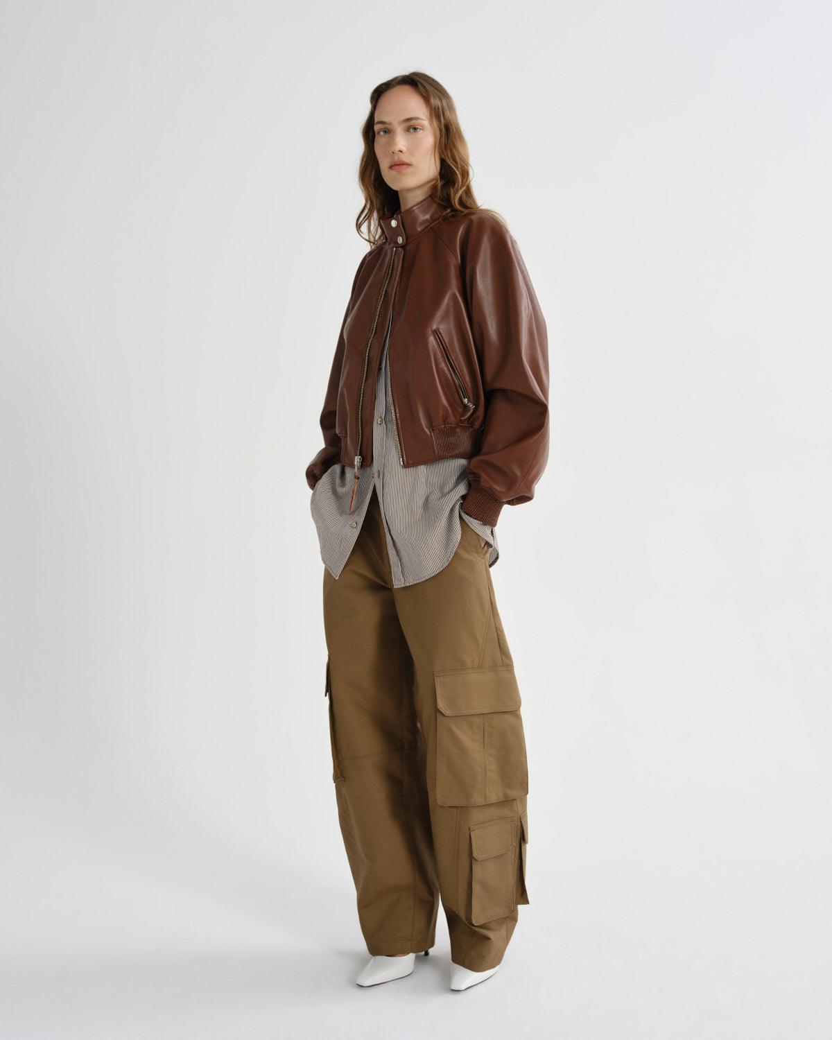 Person wearing a brown leather jacket and cargo pants on a white background