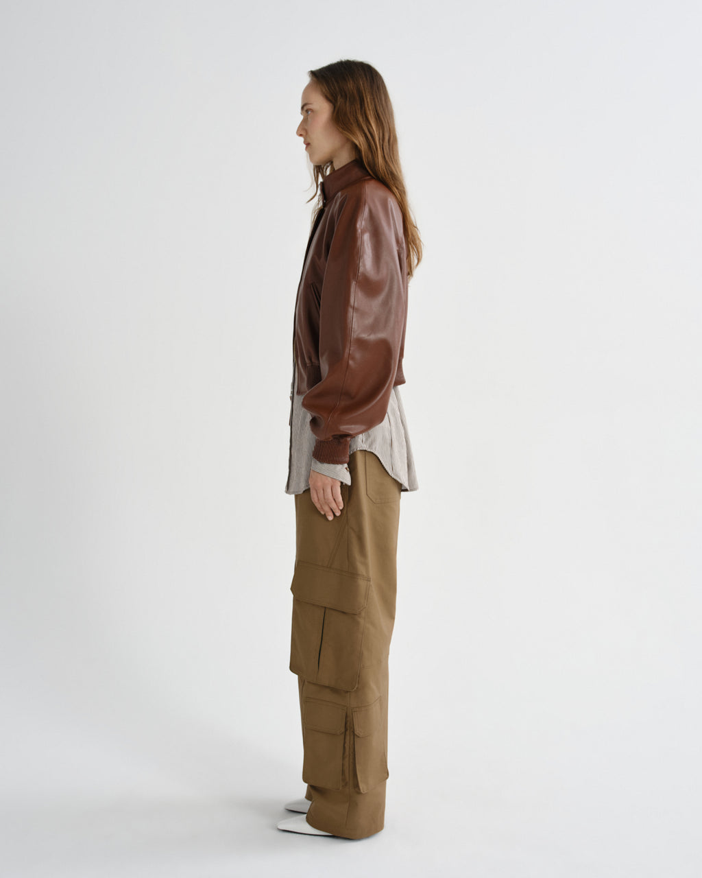 Person wearing a brown leather jacket and beige pants on a white background