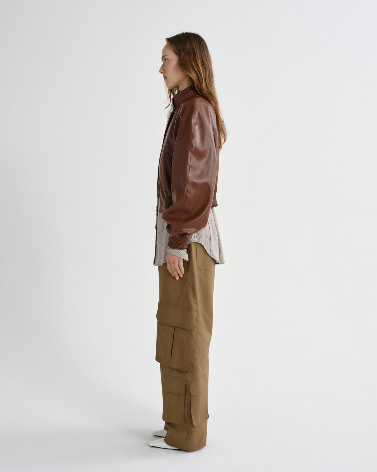 Person wearing a brown leather jacket and beige pants on a white background
