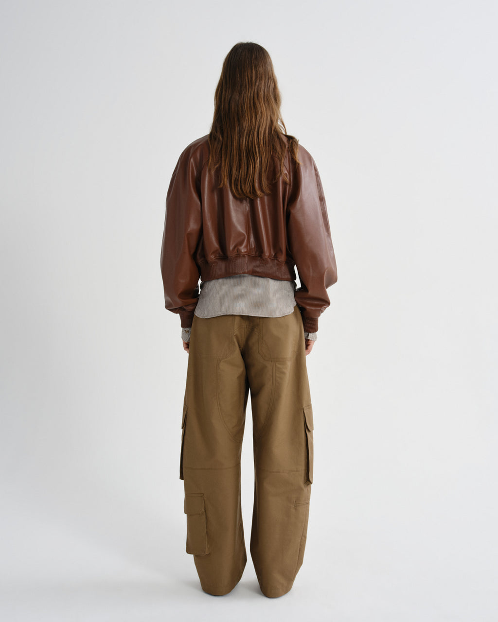 Person wearing a brown leather jacket and cargo pants on a white background