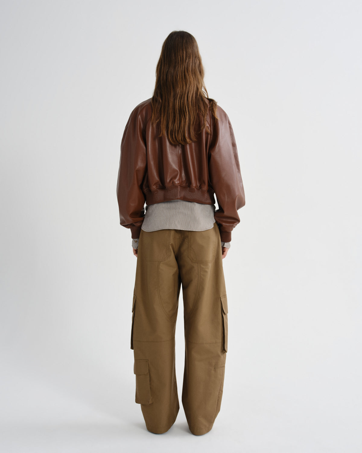 Person wearing a brown leather jacket and cargo pants on a white background