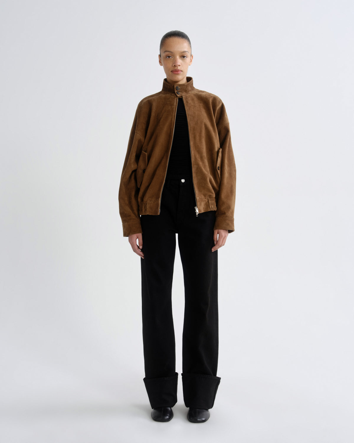 Person wearing a brown jacket and black pants on a white background