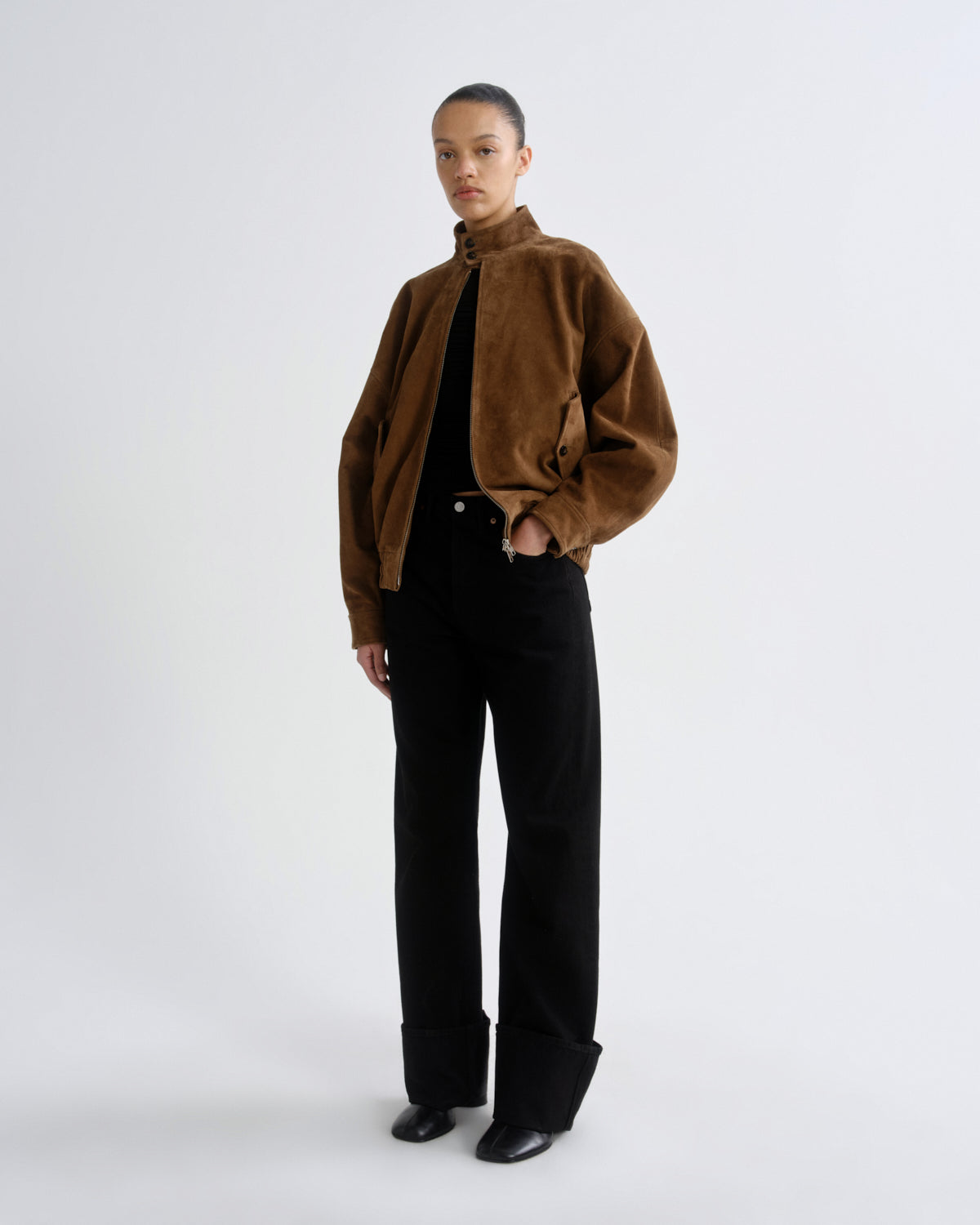 Person wearing a brown jacket and black pants on a white background