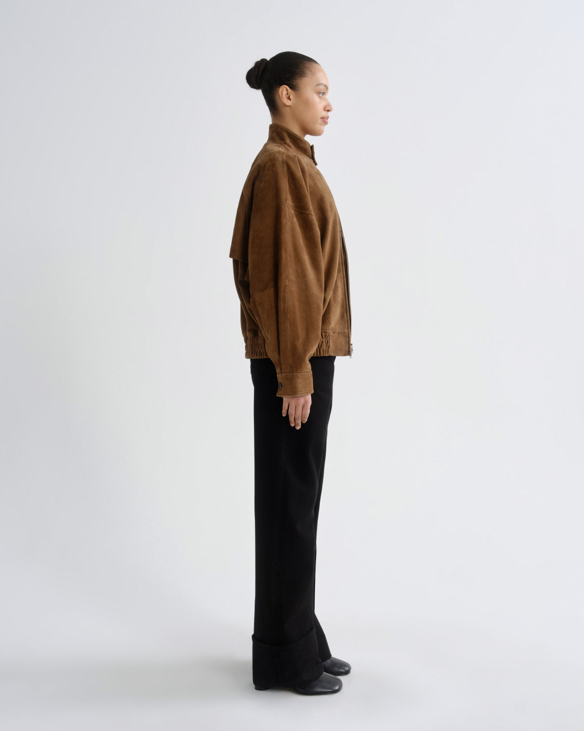 Person wearing a brown jacket and black pants on a white background