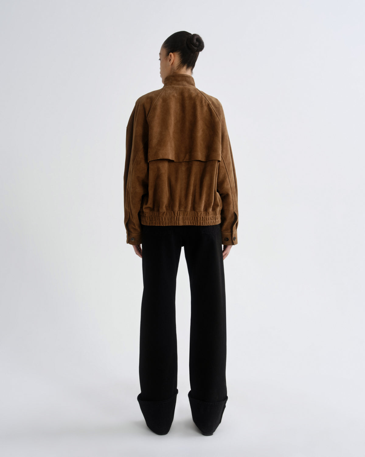Person wearing a brown jacket and black pants on a white background