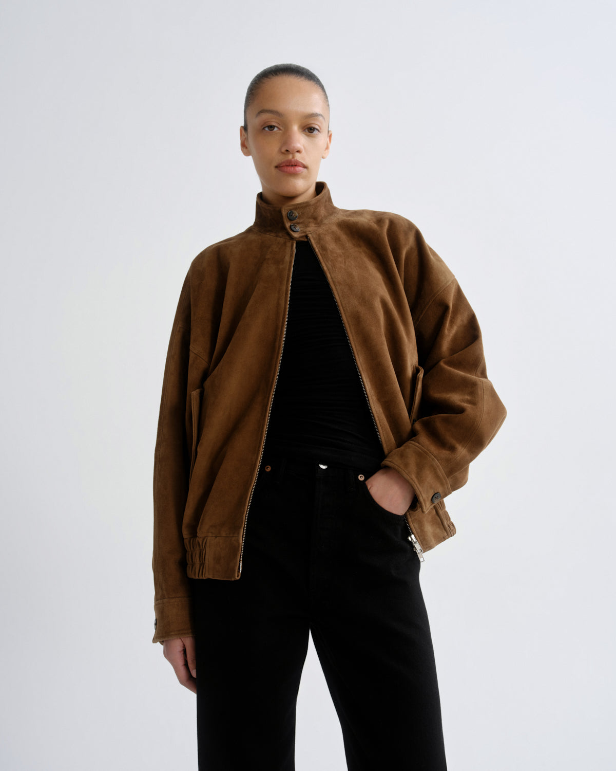 Person wearing a brown jacket and black pants on a white background