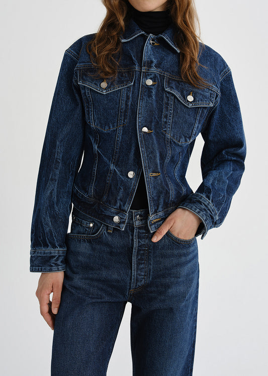 A cropped dark blue denim jacket with silver buttons, worn by a model paired with matching dark blue jeans and a black turtleneck against a grey background.