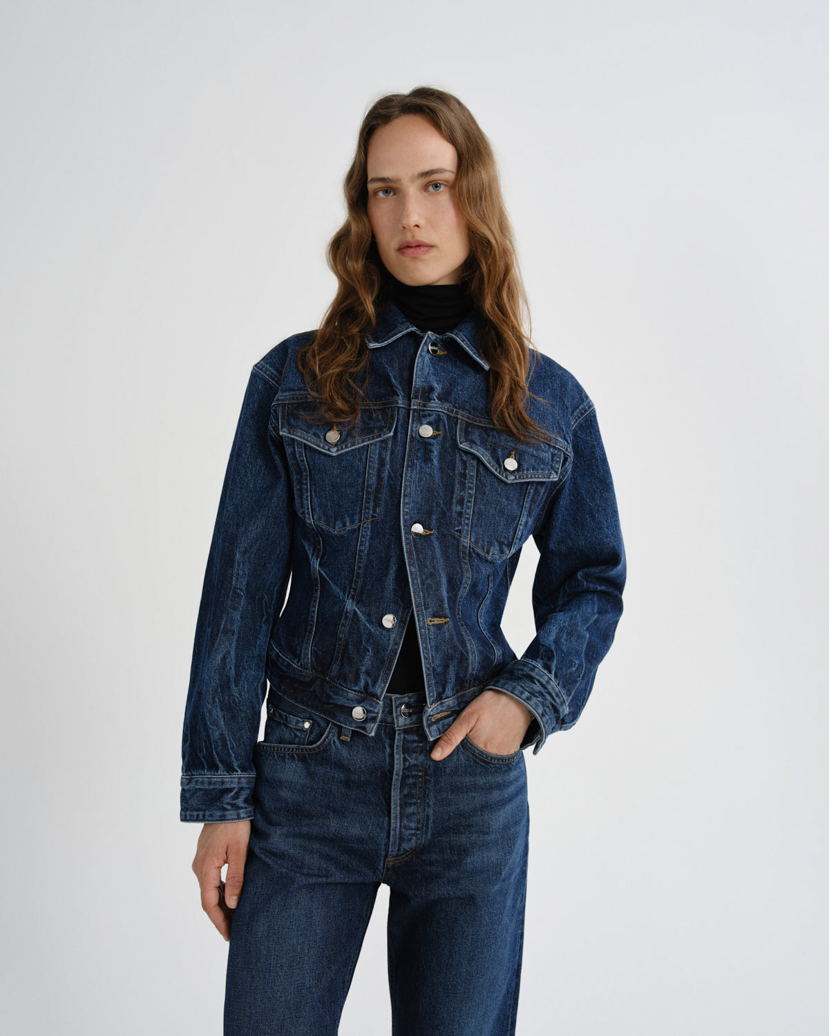 Person wearing a blue denim jacket and jeans on a white background
