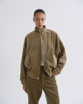 A model wearing a brown corduroy jacket and matching corduroy pants over a striped top, photographed against a plain light gray studio background.