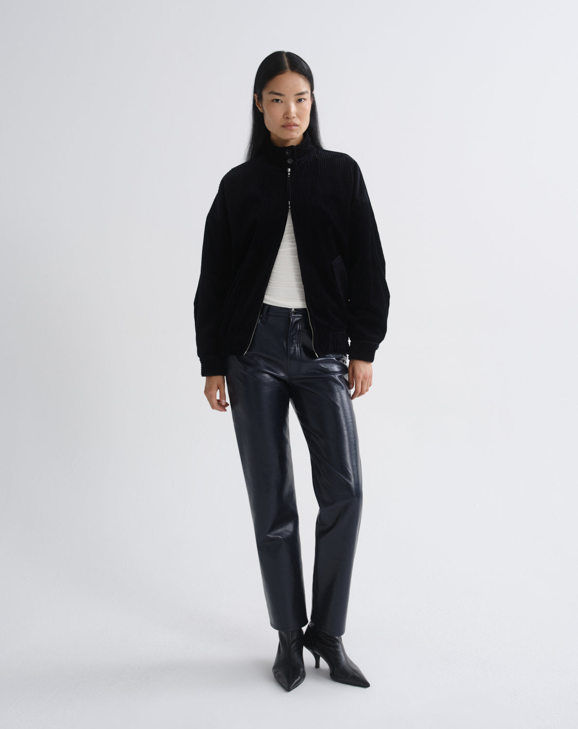 Person wearing a black bomber jacket with dark grey straight leg leather pants on a grey background