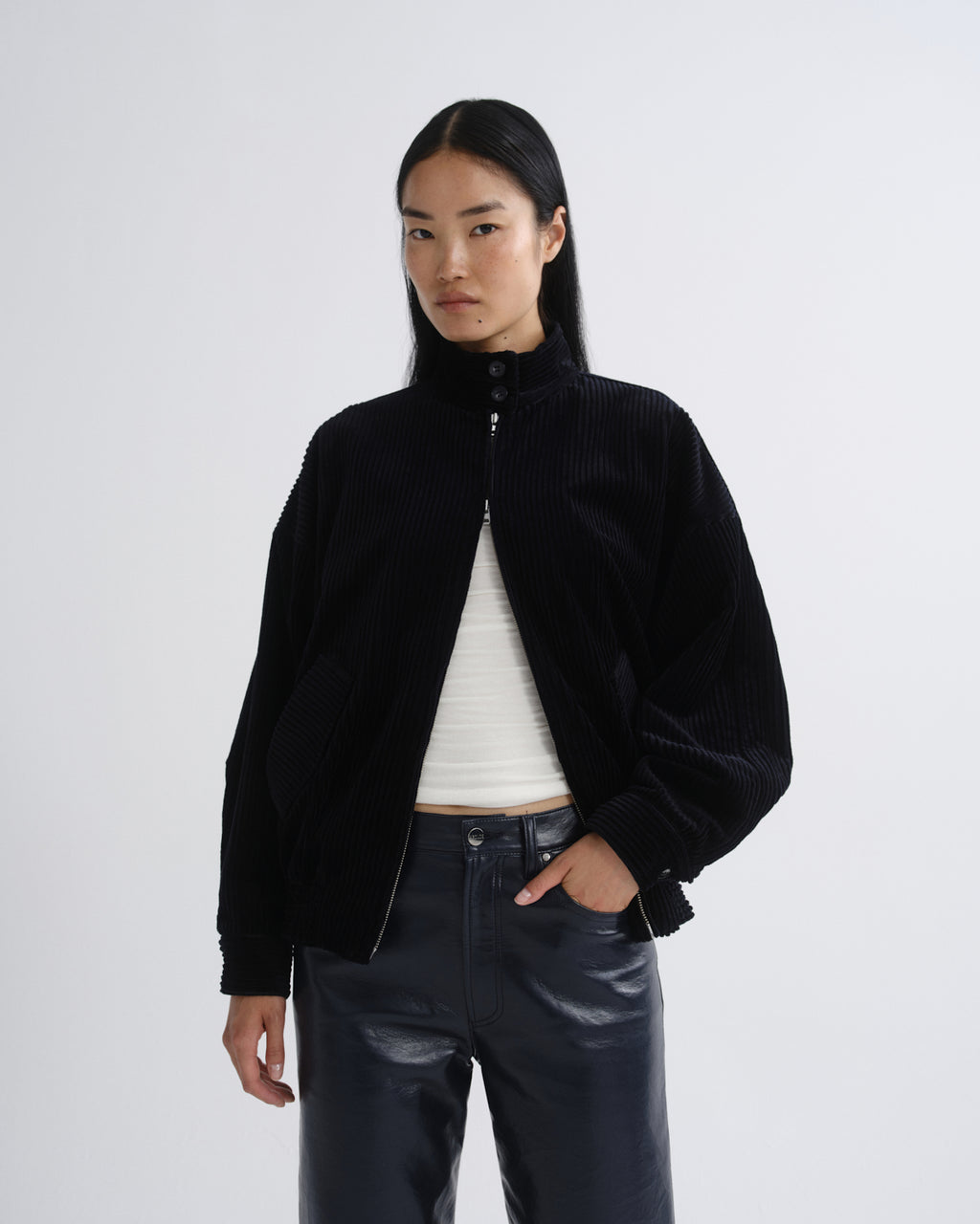 Person wearing a black bomber jacket with dark grey straight leg leather pants on a grey background