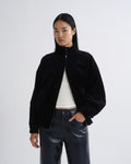 Person wearing a black bomber jacket with dark grey straight leg leather pants on a grey background