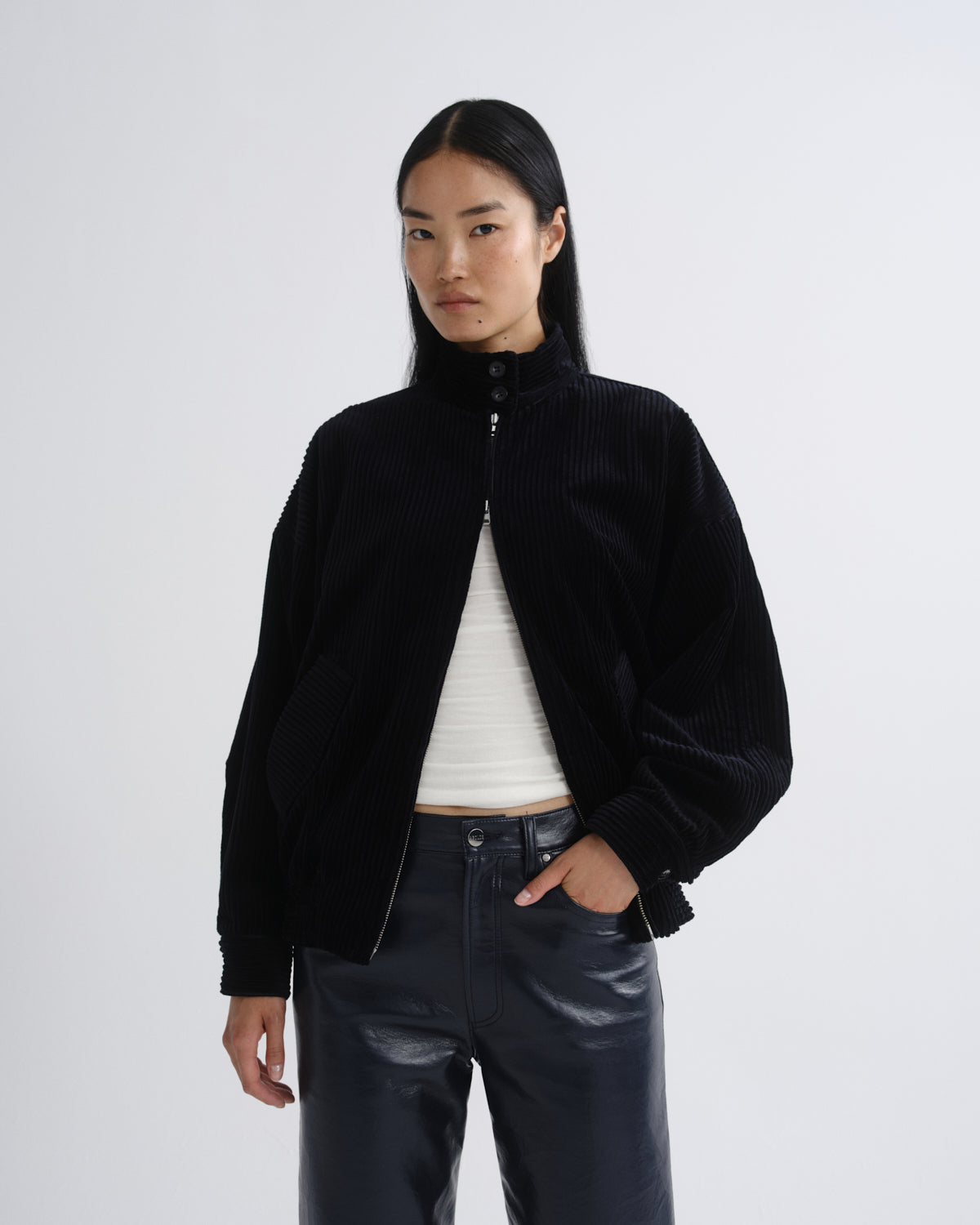 Person wearing a black bomber jacket with dark grey straight leg leather pants on a grey background