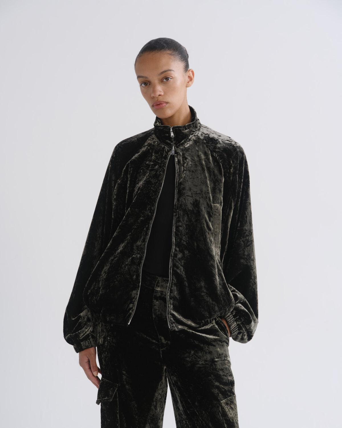 Woman wearing a black velvet long sleeve top with black velvet pants on a grey background.