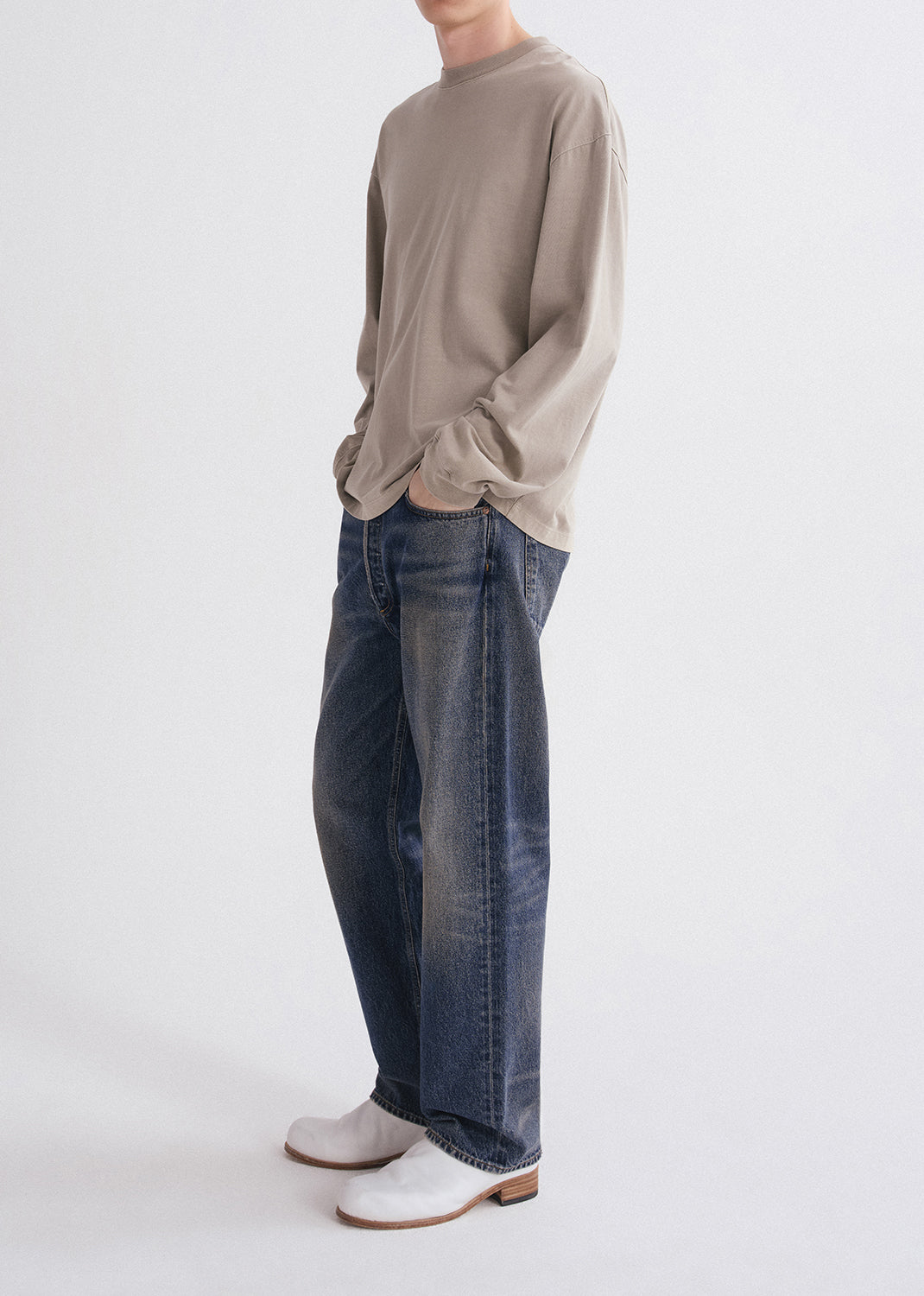 Person wearing a beige long-sleeve shirt and blue jeans on a white background