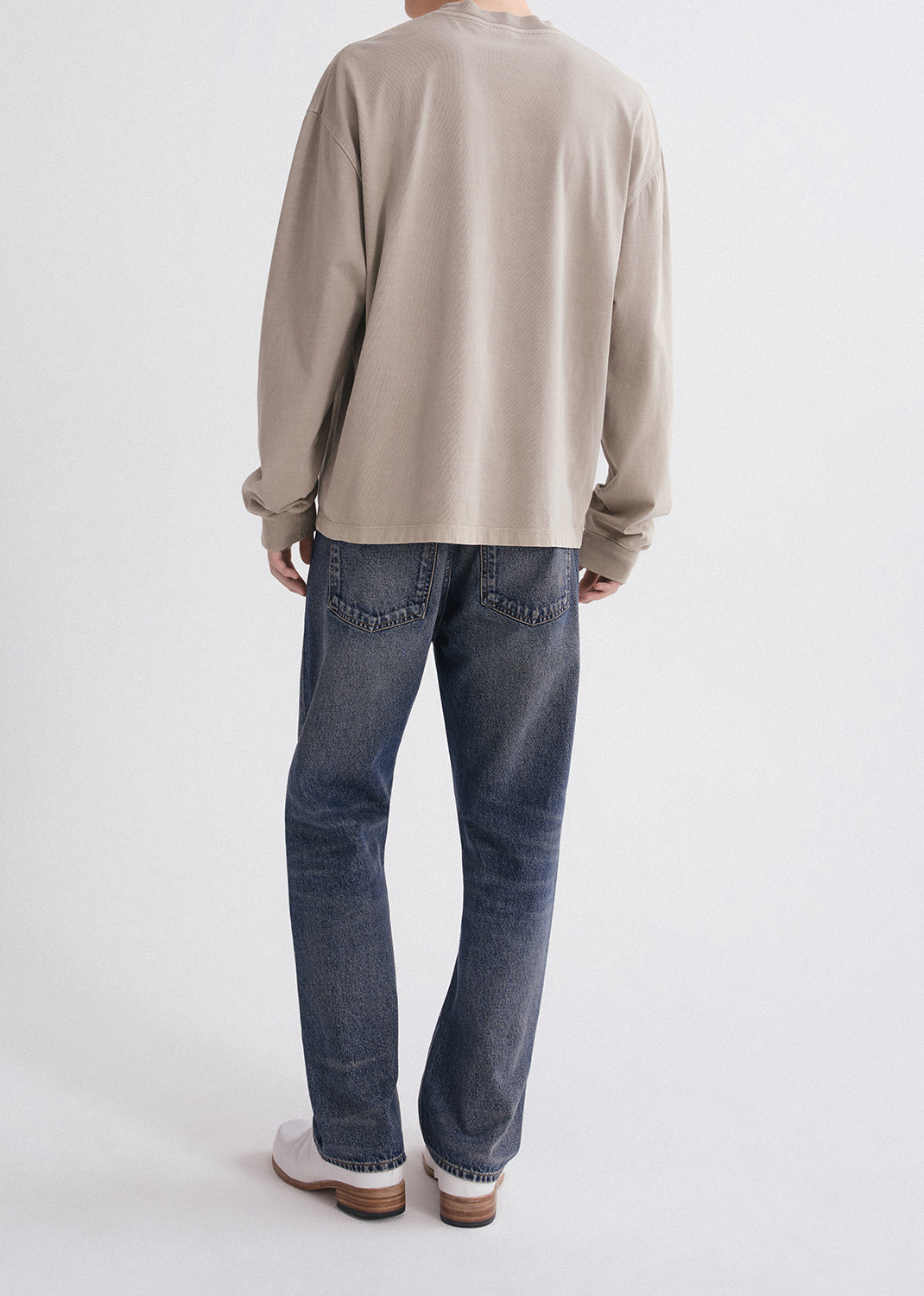Person wearing a beige long-sleeve shirt and blue jeans on a white background