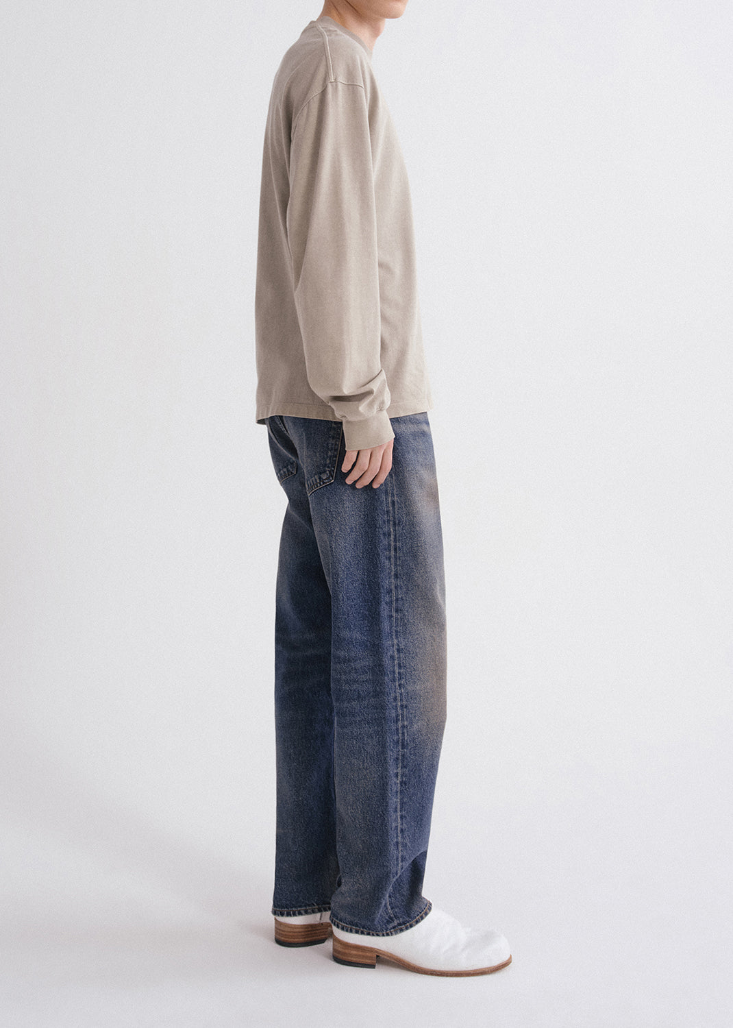 Person wearing a beige long-sleeve shirt and blue jeans on a white background