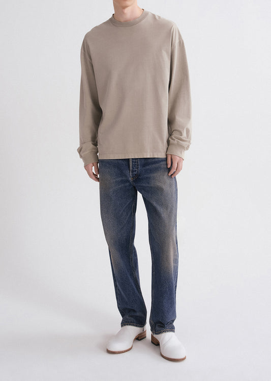 Person wearing a beige long-sleeve shirt and blue jeans on a white background