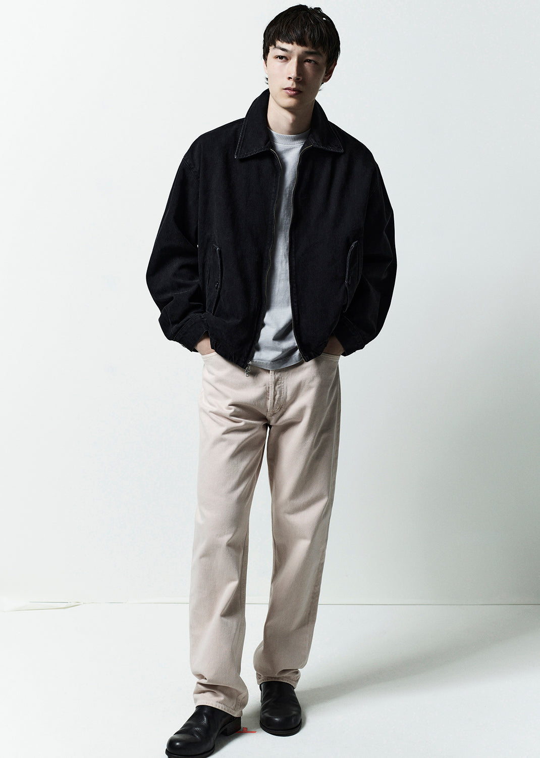Man wearing a black jacket, white shirt, beige pants, and black shoes on a white background