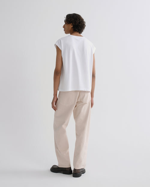 A model shown from the back wearing a white sleeveless t-shirt and beige trousers, standing against a plain light gray studio background.