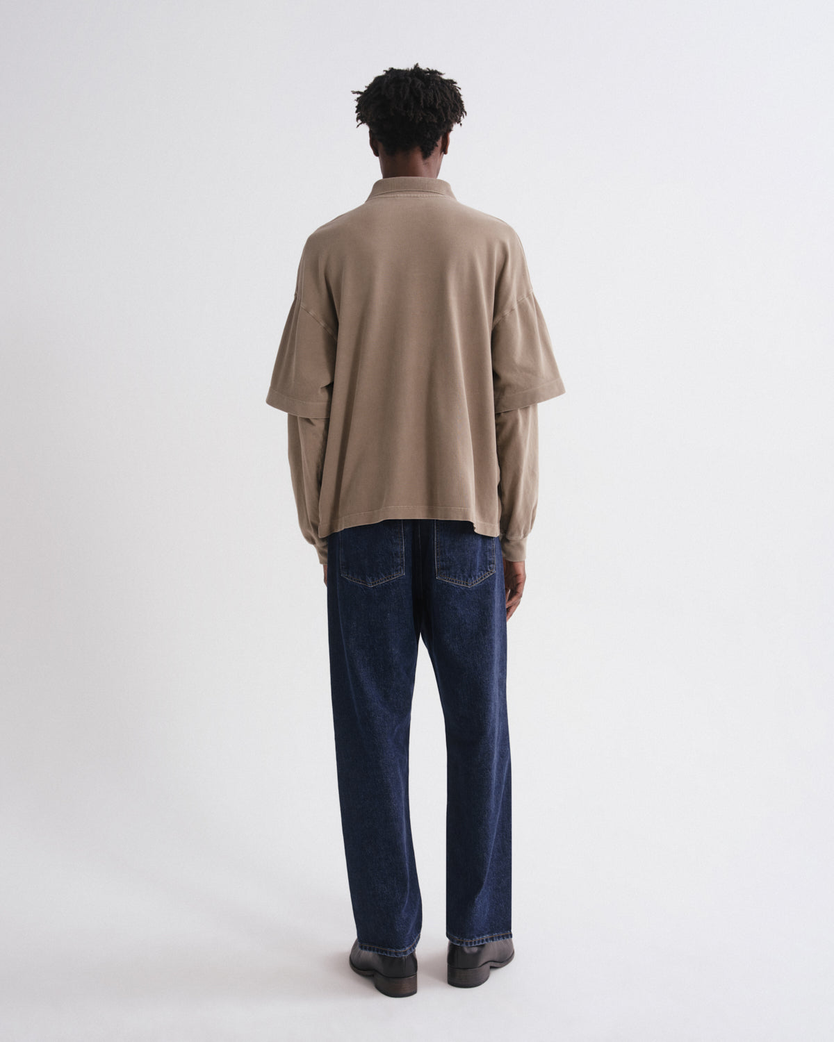 A model viewed from behind wearing a beige oversized long-sleeve knit top and dark blue straight-leg jeans against a plain white studio background.