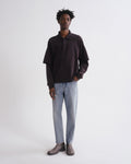 Person wearing a dark brown long-sleeve shirt and light blue jeans on a white background