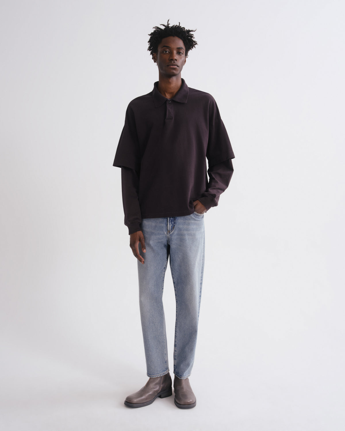 Person wearing a dark brown long-sleeve shirt and light blue jeans on a white background