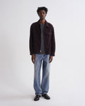 Man wearing a dark brown jacket, gray shirt, and blue jeans on a white background