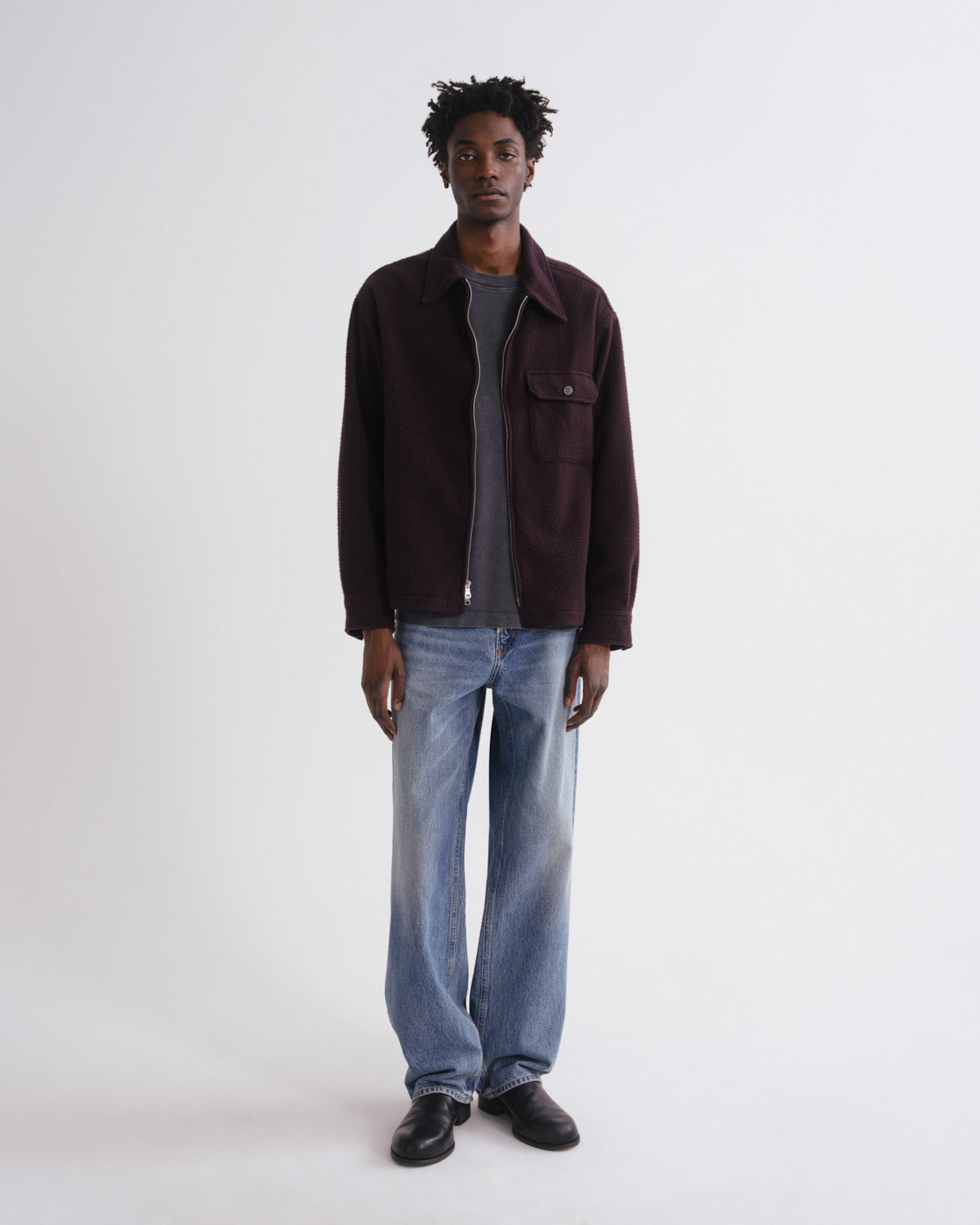 Man wearing a dark brown jacket, gray shirt, and blue jeans on a white background