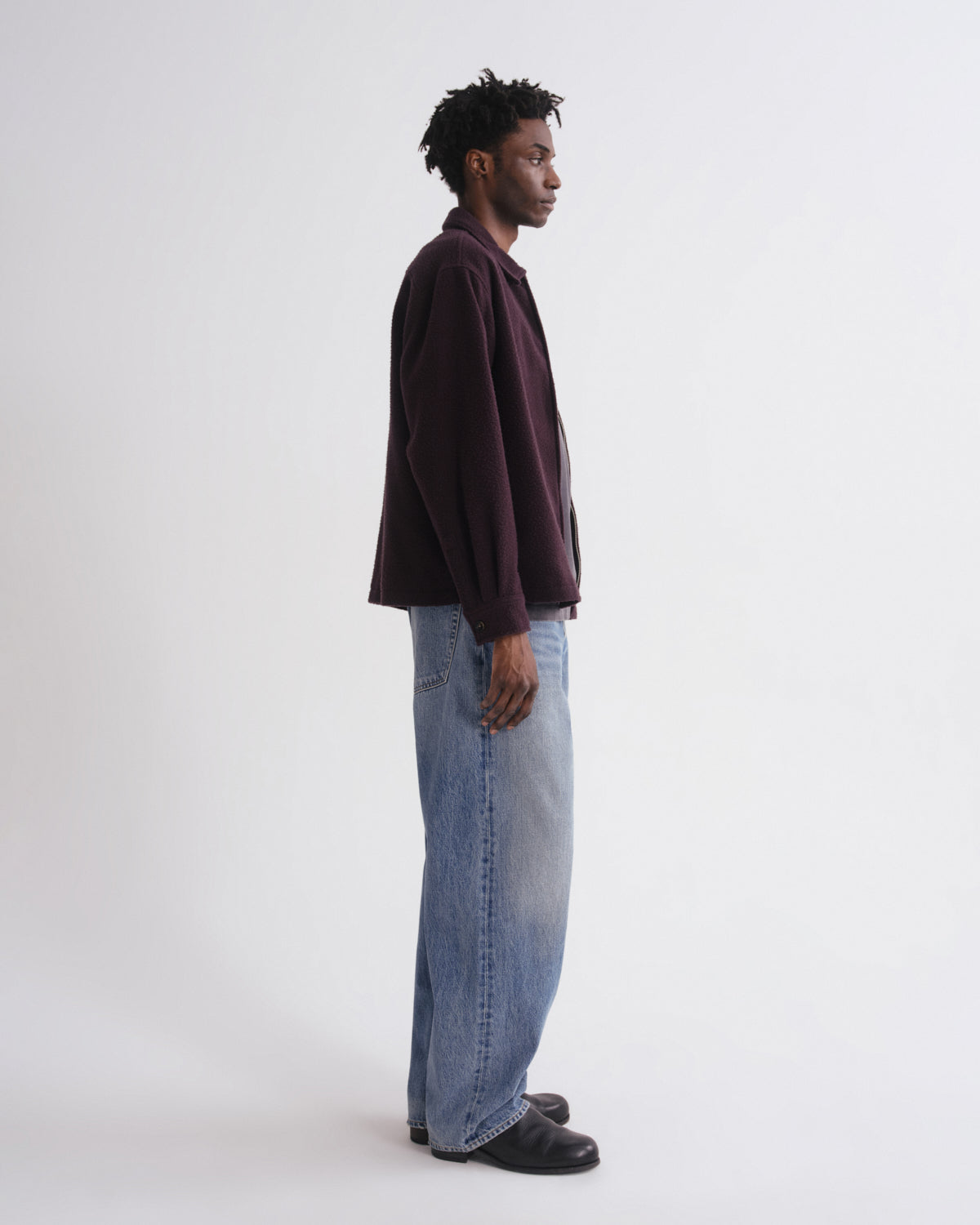 Man wearing a dark shirt and light blue jeans standing against a white background