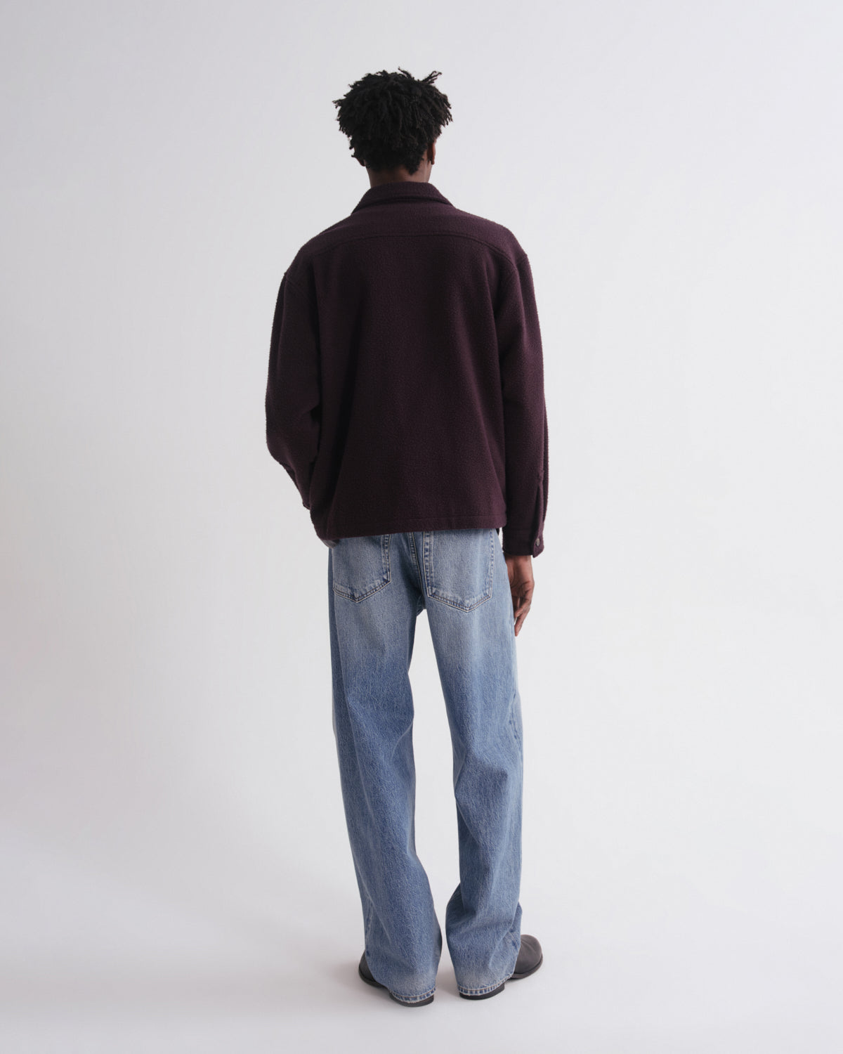 Person wearing a dark brown sweater and light blue jeans on a white background