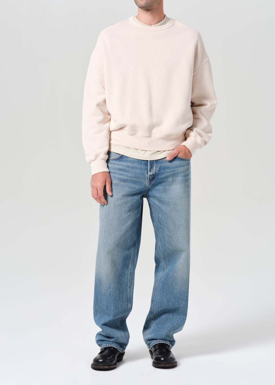 Person wearing a beige sweater and blue jeans on a white background
