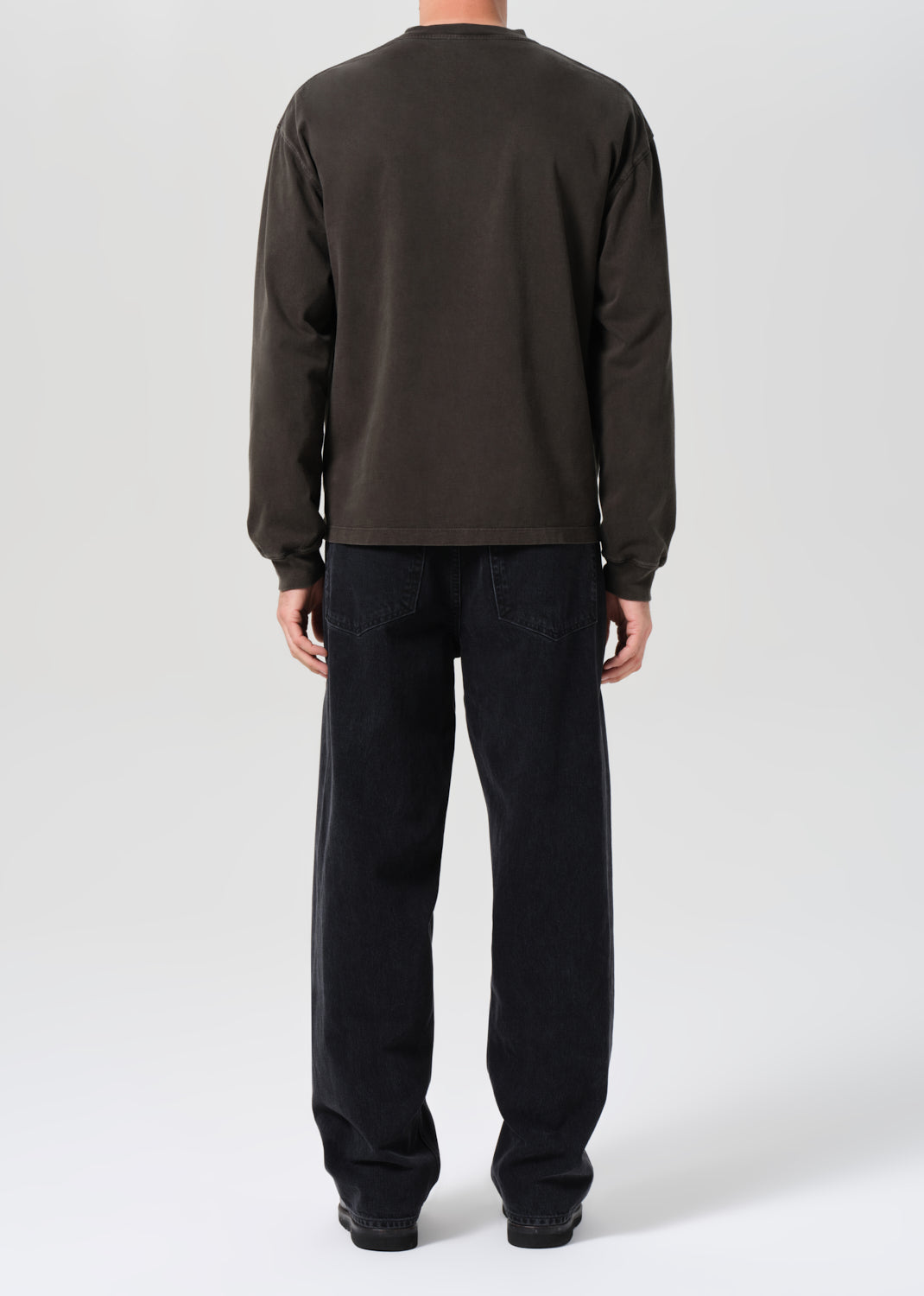 Person wearing a dark long-sleeve shirt and black pants on a white background