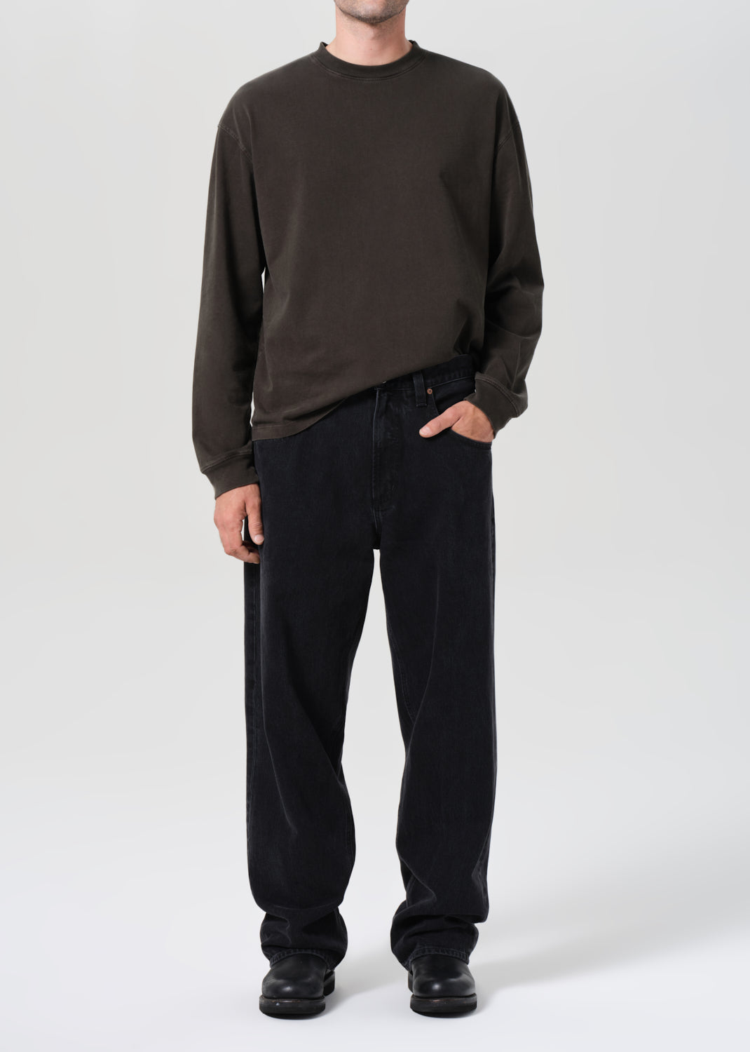 Person wearing a dark brown long-sleeve shirt and black pants on a white background