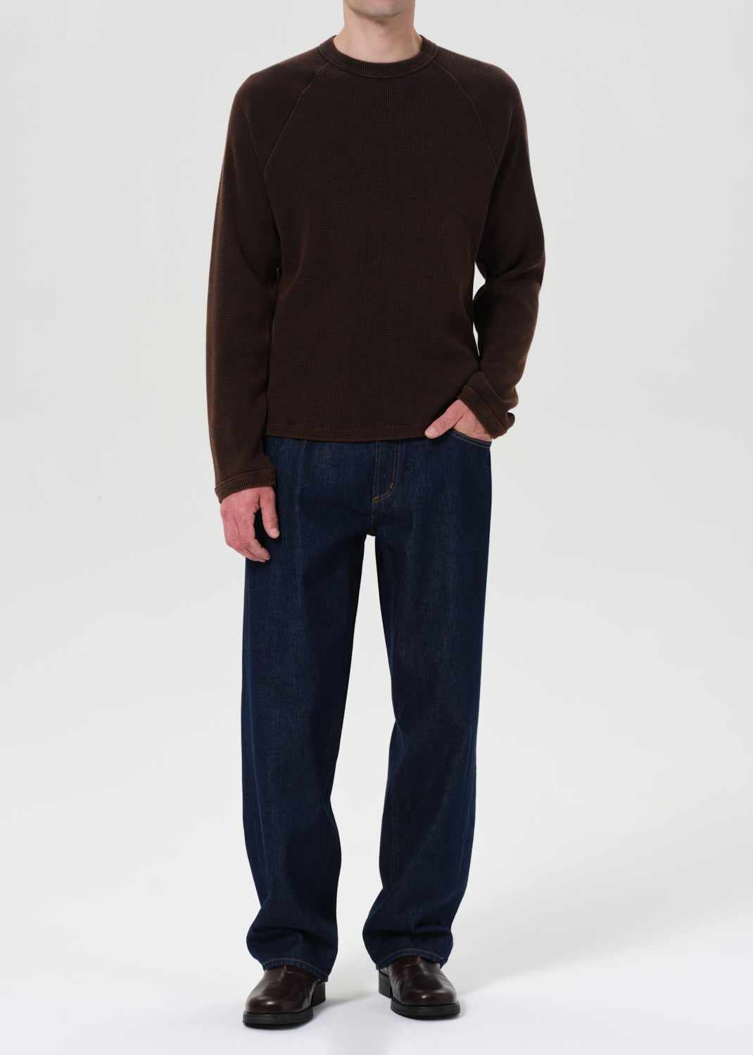 Person wearing a brown sweater and dark blue jeans on a white background