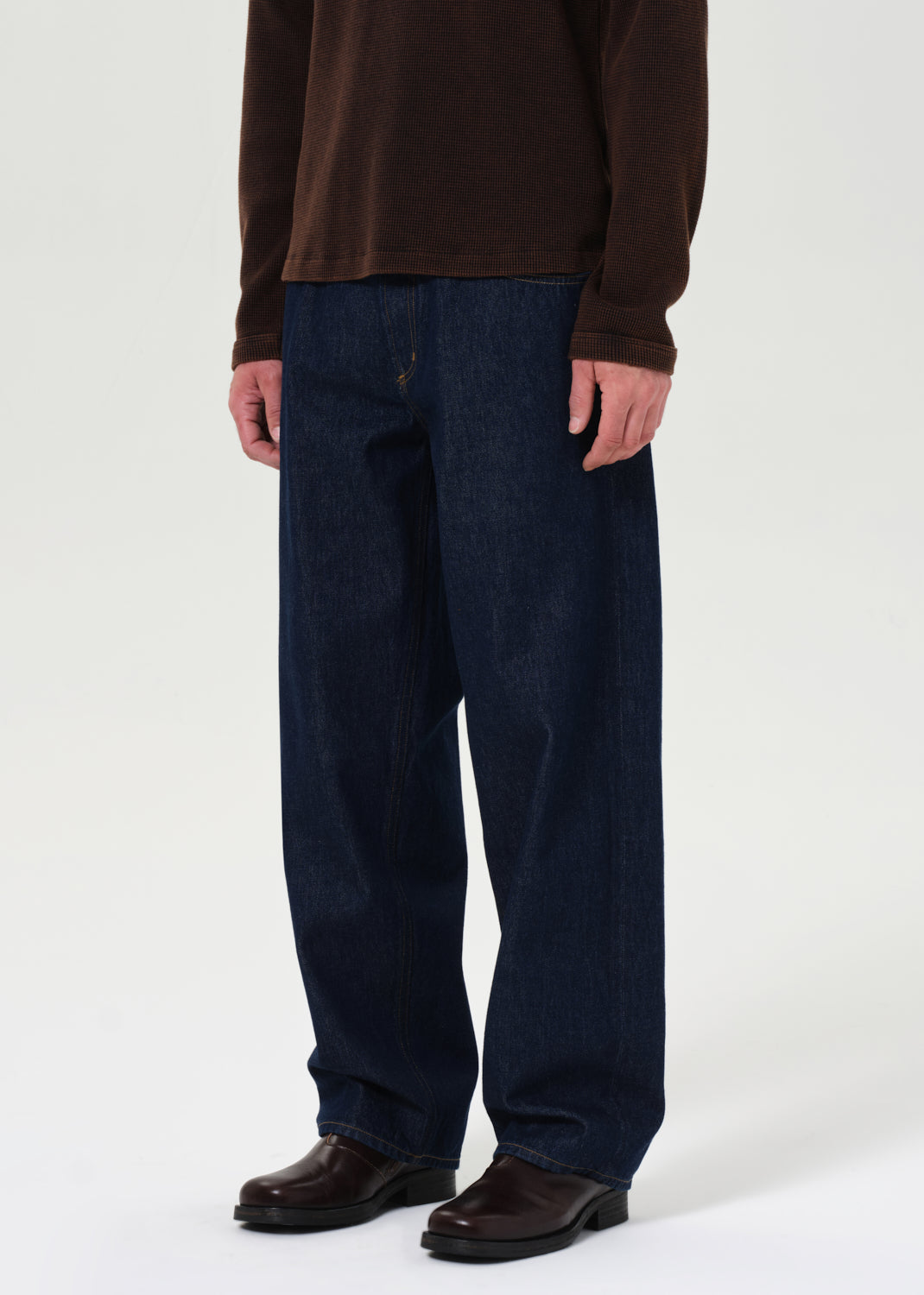 Person wearing dark blue jeans and a brown shirt on a white background