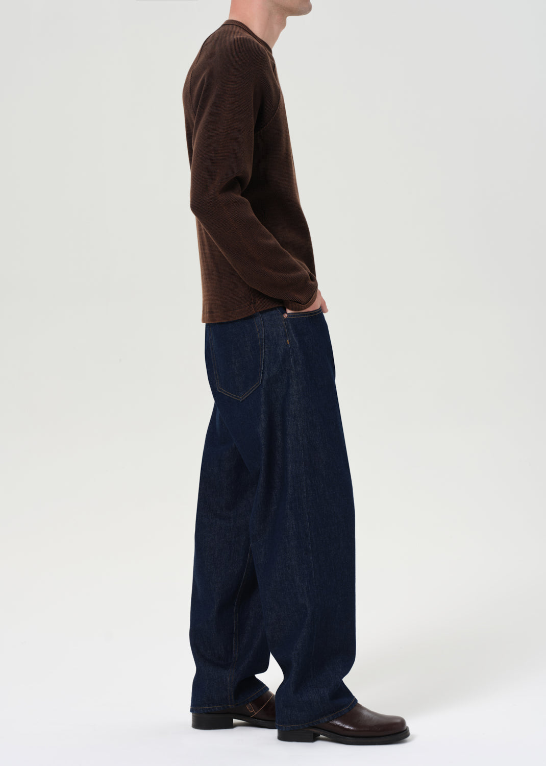 Person wearing a brown sweater and dark blue wide-leg pants on a white background