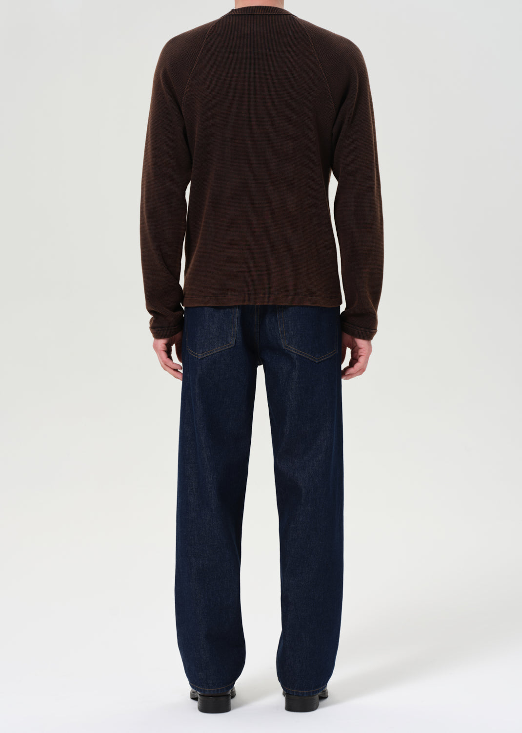 Person wearing a brown long-sleeve shirt and dark blue jeans on a white background