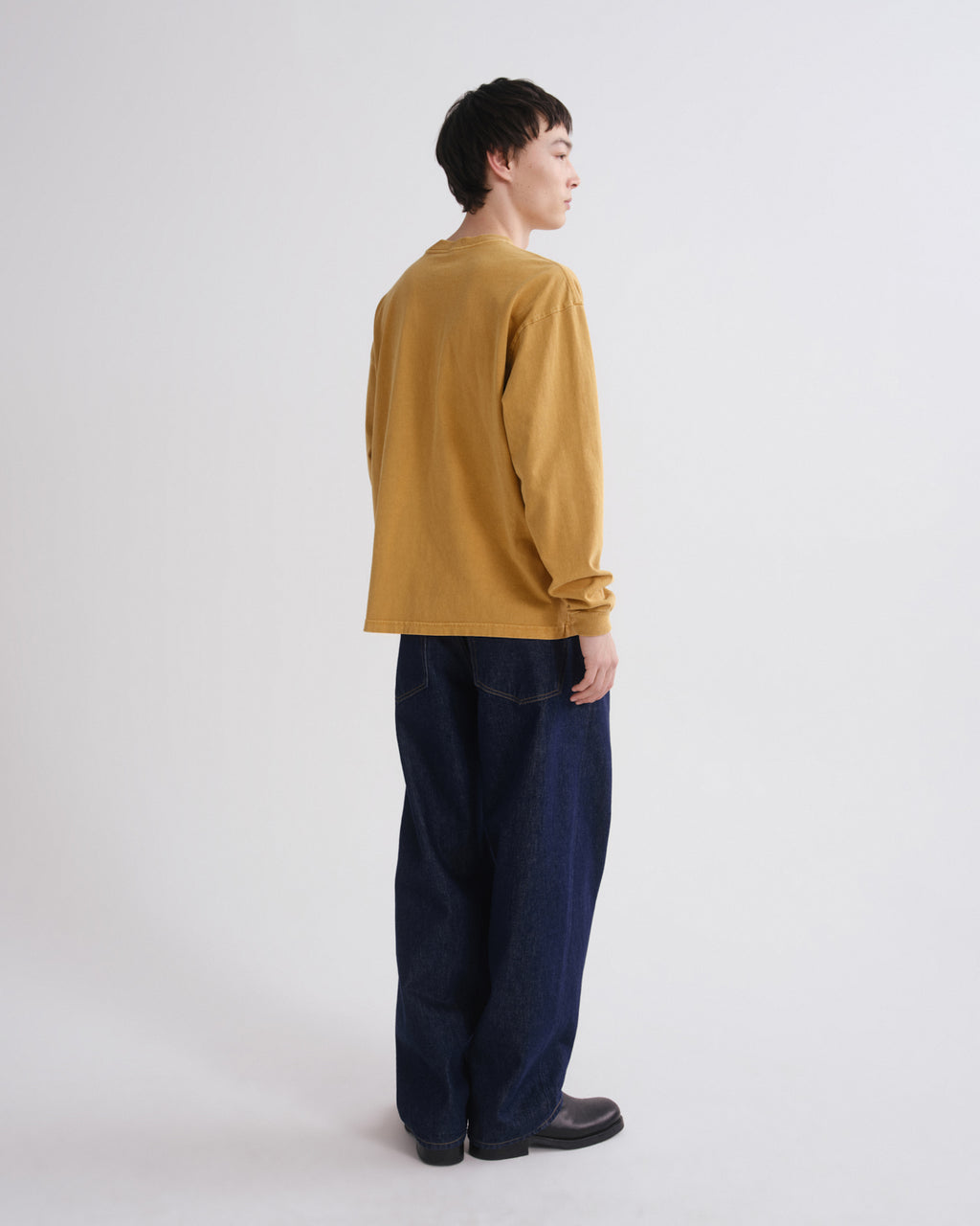 A model shown from the back wearing a mustard yellow long-sleeve shirt and dark blue wide-leg jeans against a plain light gray background.