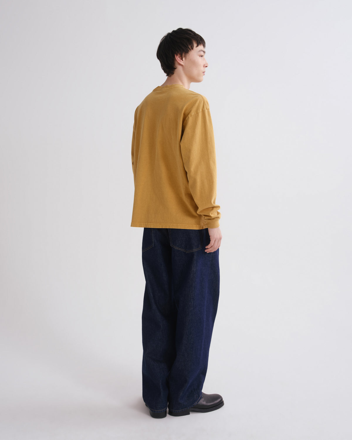 A model shown from the back wearing a mustard yellow long-sleeve shirt and dark blue wide-leg jeans against a plain light gray background.