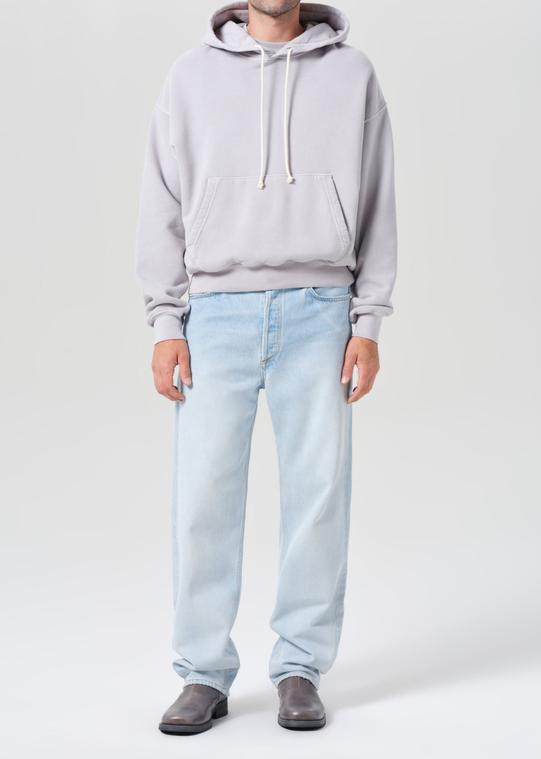 Person wearing a light gray hoodie and light blue jeans on a white background