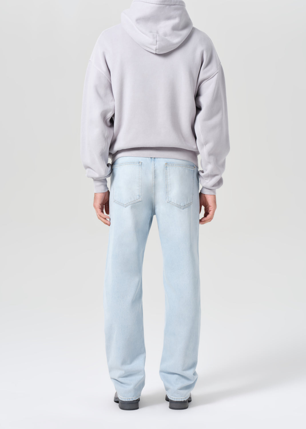 Person wearing a light gray hoodie and light blue jeans on a white background