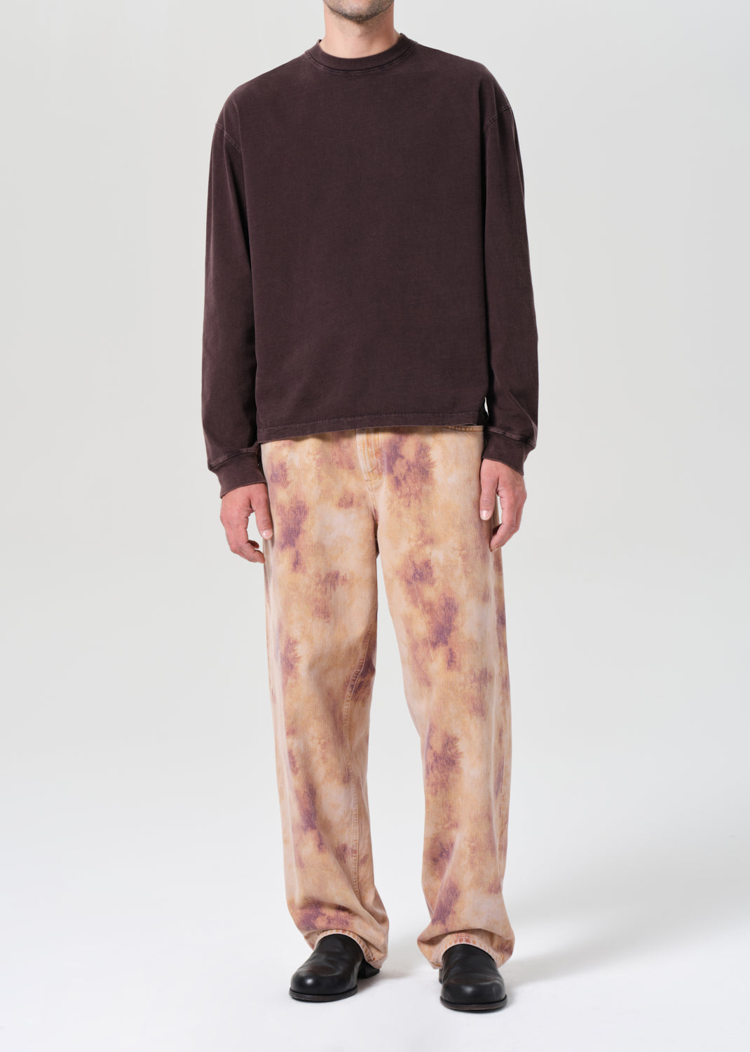 Person wearing a brown sweater and tie-dye pants on a white background