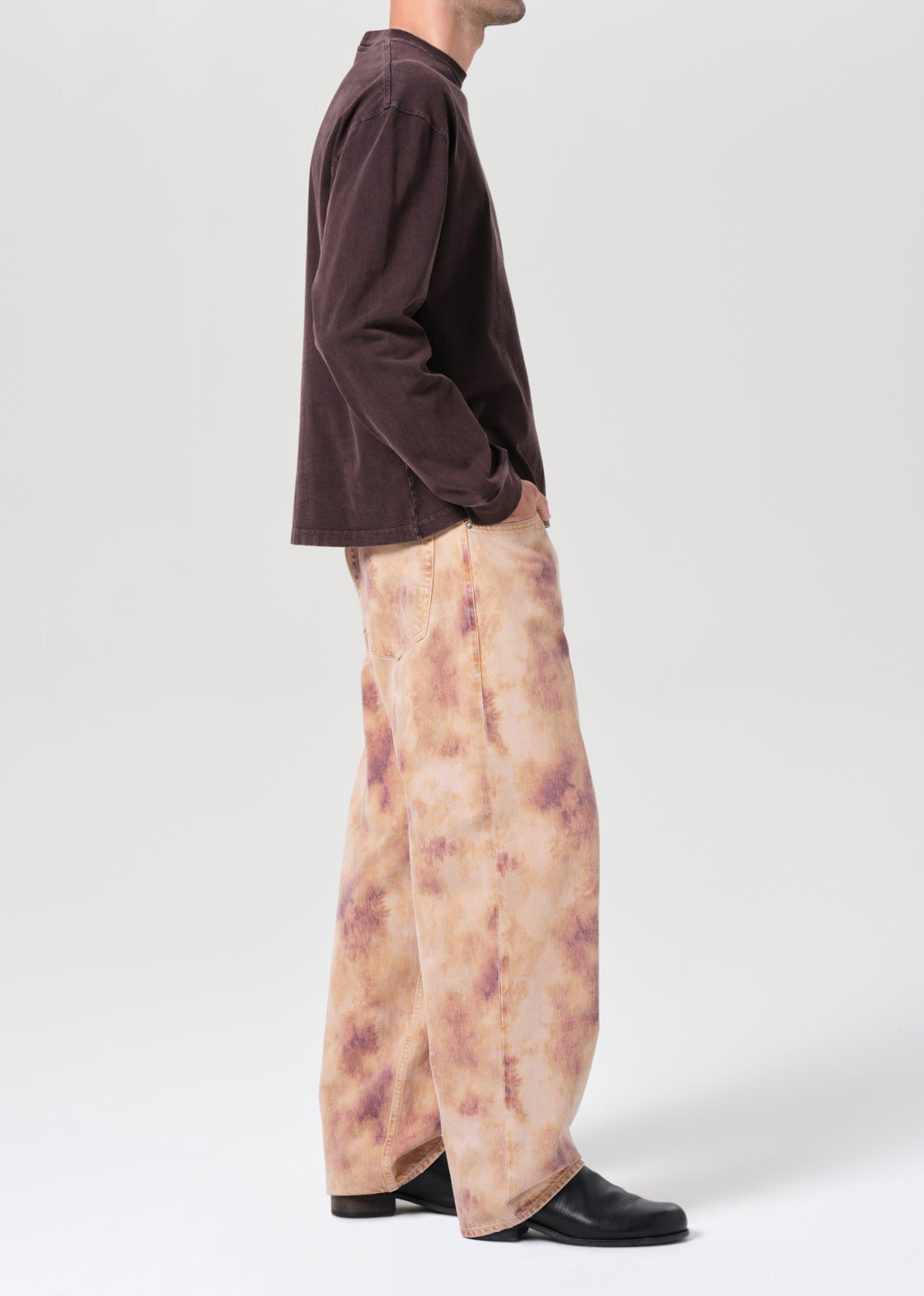 Person wearing a brown long-sleeve shirt and patterned pants on a white background