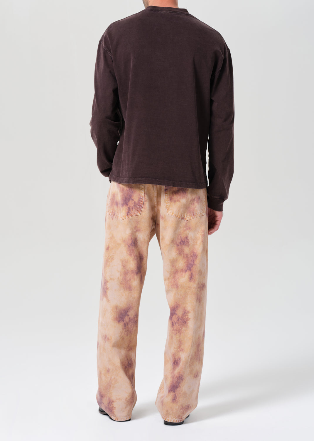 Person wearing a brown long-sleeve shirt and patterned pants on a white background