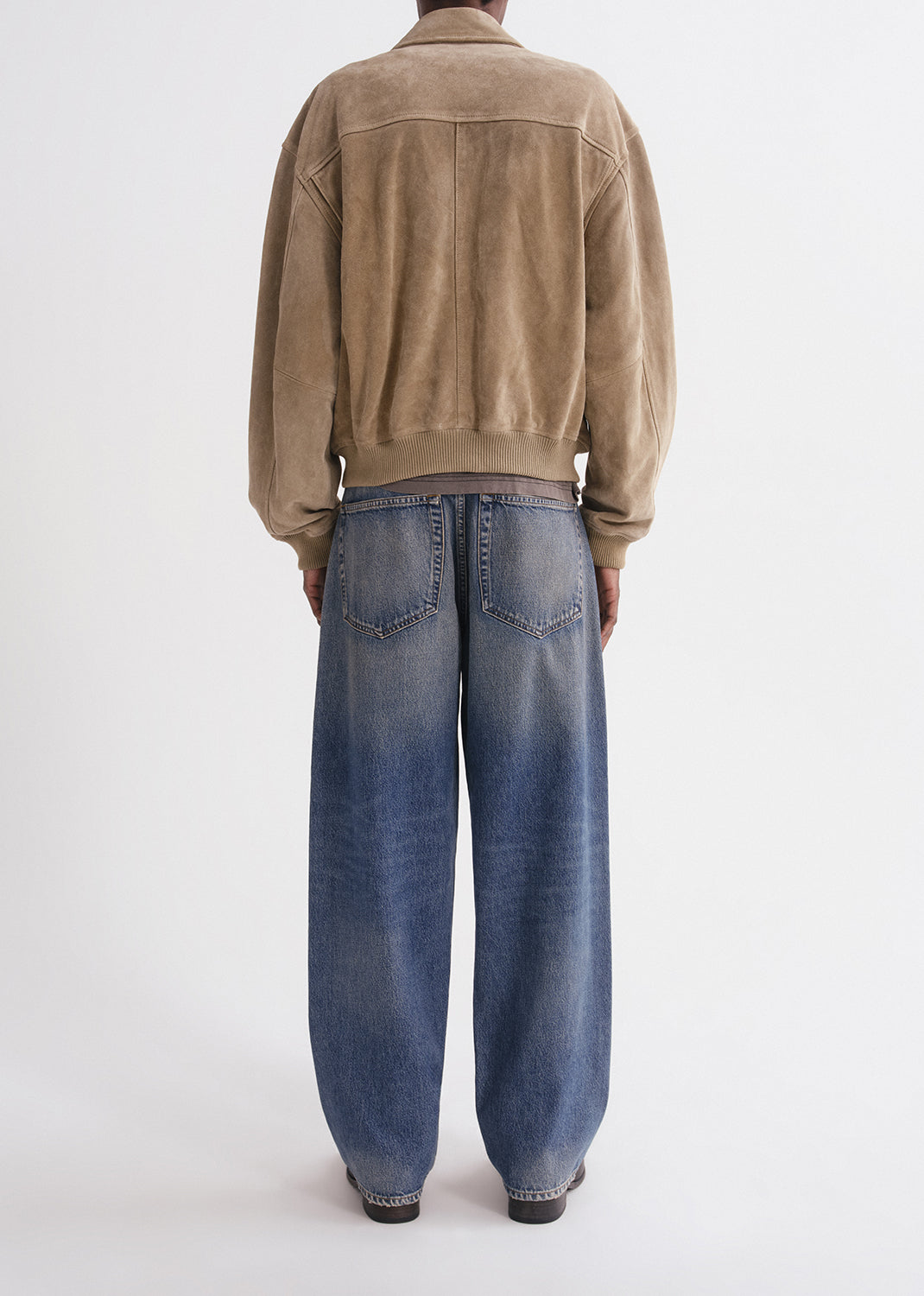 Person wearing a beige jacket and blue jeans on a grey background