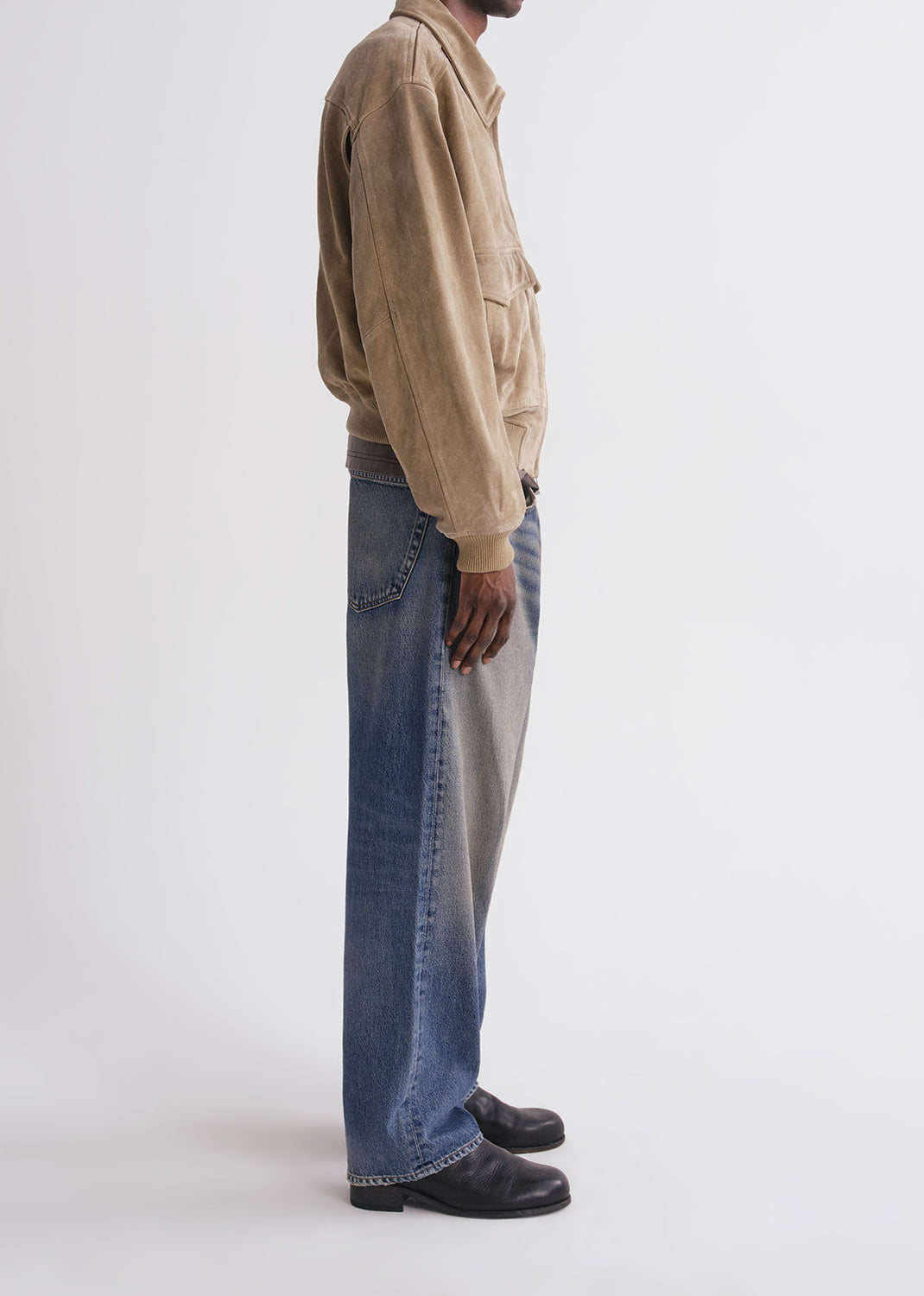 Person wearing a beige jacket and blue jeans on a grey background