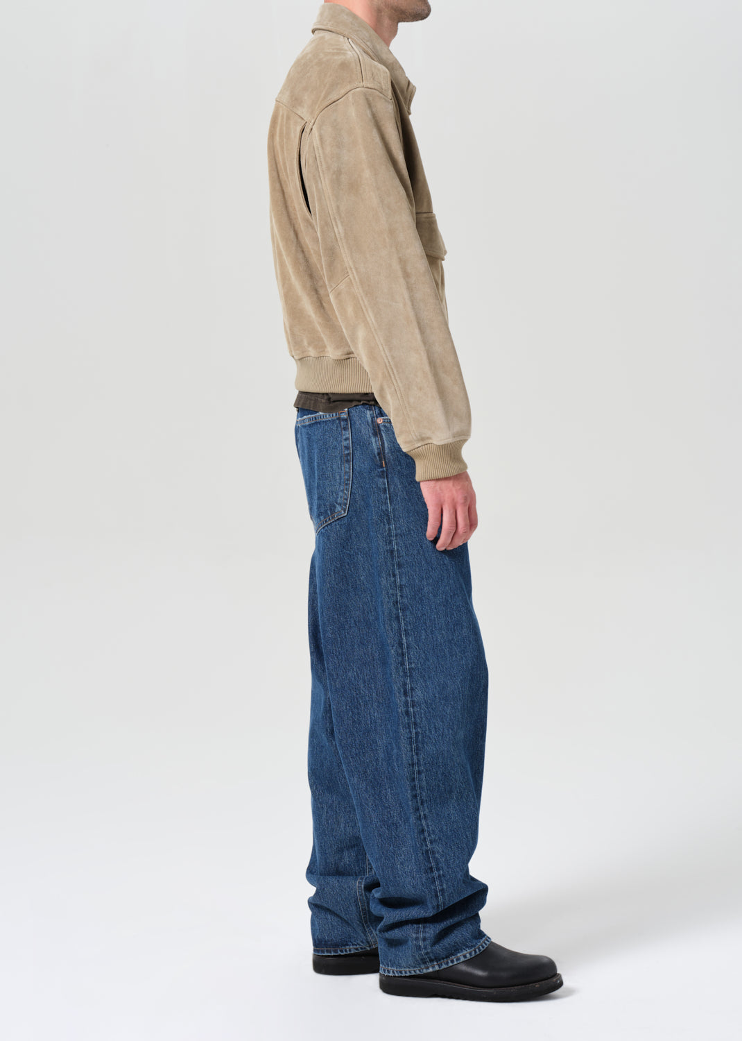 Person wearing a beige jacket and blue jeans on a white background