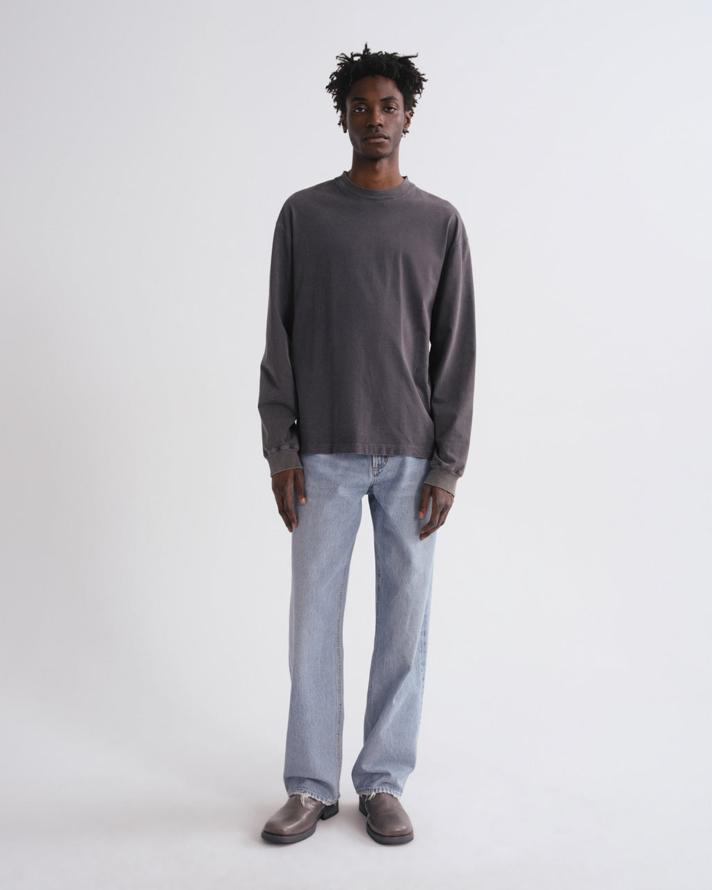 Man wearing a dark gray long-sleeve shirt and light blue jeans on a white background