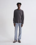 Man wearing a dark gray long-sleeve shirt and light blue jeans on a white background